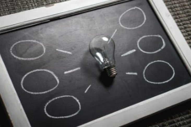 Blackboard with a light bulb ontop of it with chalk bubbles radiating from bulb