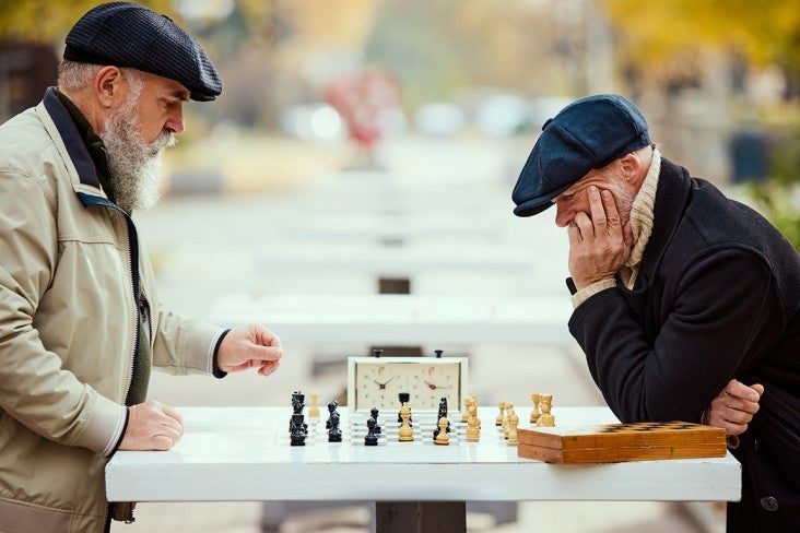 Two older men play chess outdoors