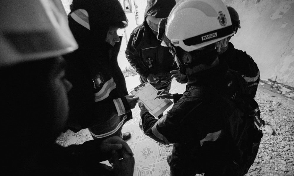 four people in hard hats look at a clipboard in a partly demolished building