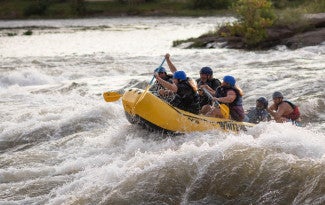 People in a yellow inflatable boat paddle on river rapids