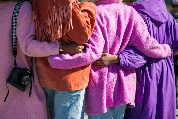 Four people standing in a line with arms linked together behind their backs