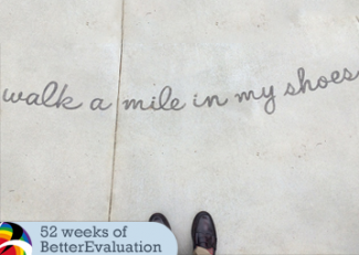 Walk a mile in my shoes is handwritten on the pavement in front of a pair of formal shoes