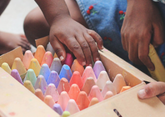 a child's hand reaches into a box of large chalks